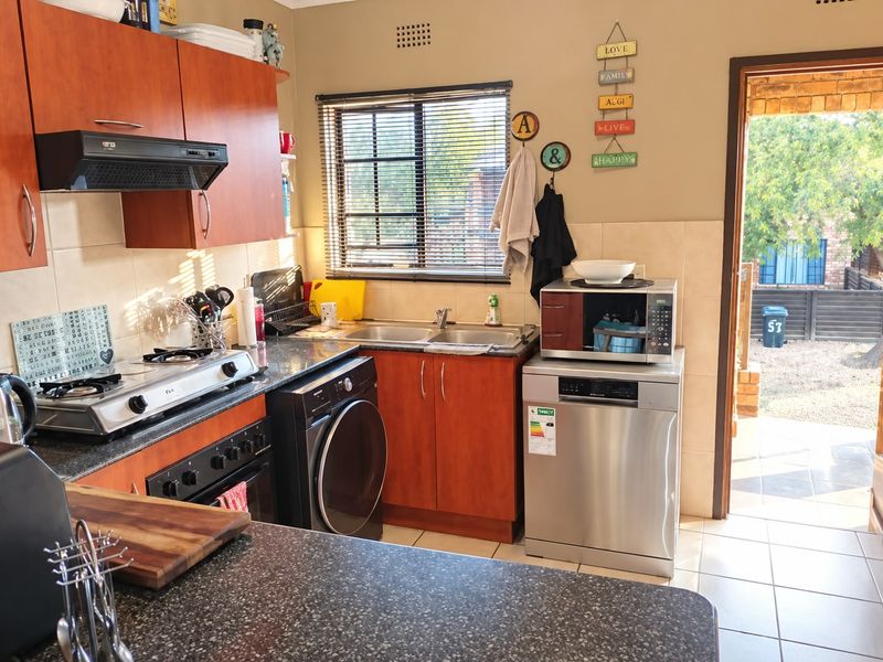 Functional kitchen featuring wood-finish cabinetry, granite countertops, a double basin sink, and a tiled backsplash with direct access to the exterior.