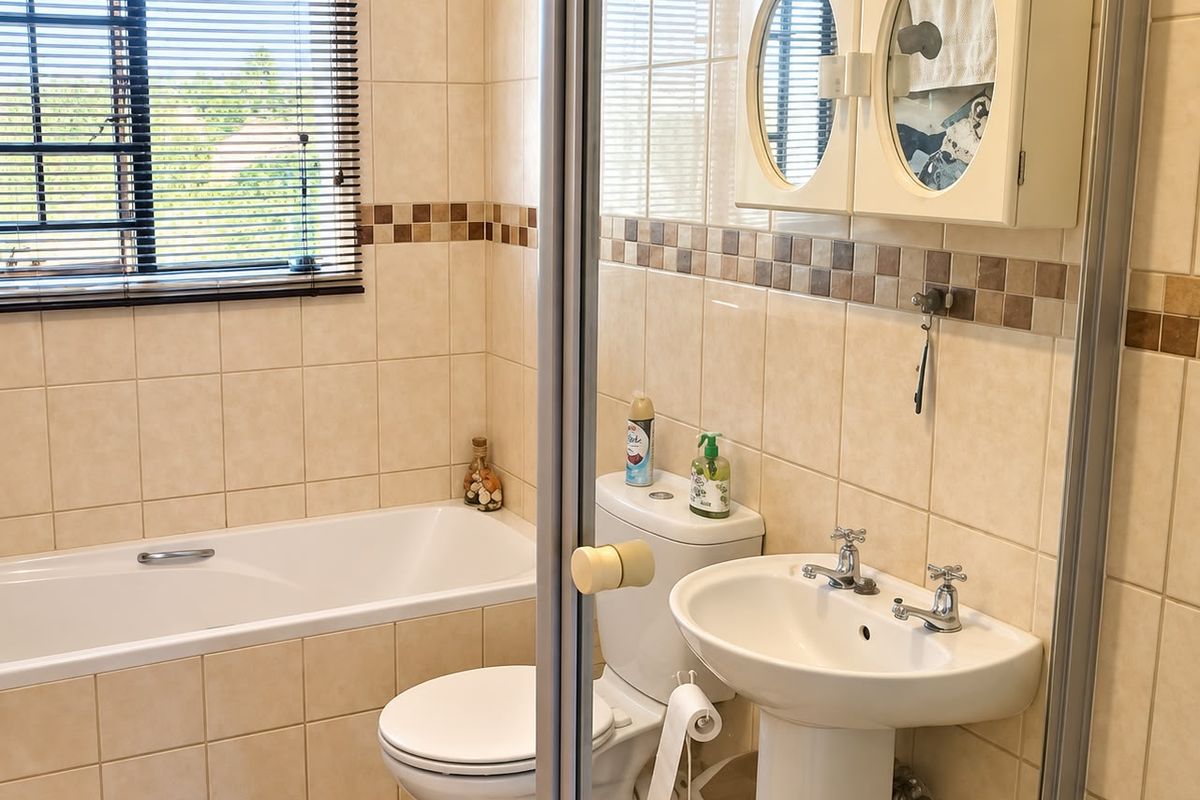A functional bathroom featuring a bathtub, pedestal basin, toilet, and tiled finishes, offering a clean and practical layout.