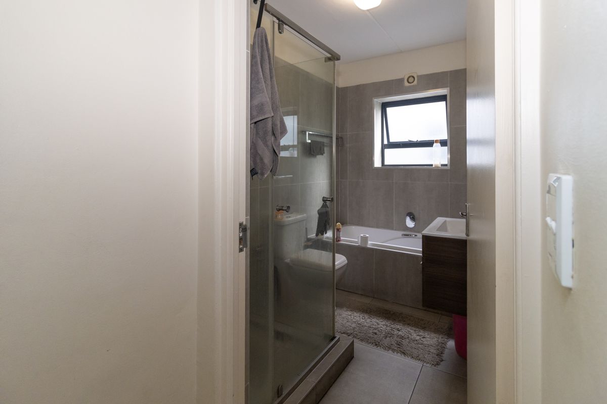 A functional bathroom featuring a glass shower enclosure, a built-in bathtub, and a modern wall-mounted vanity with tiled finishes throughout.