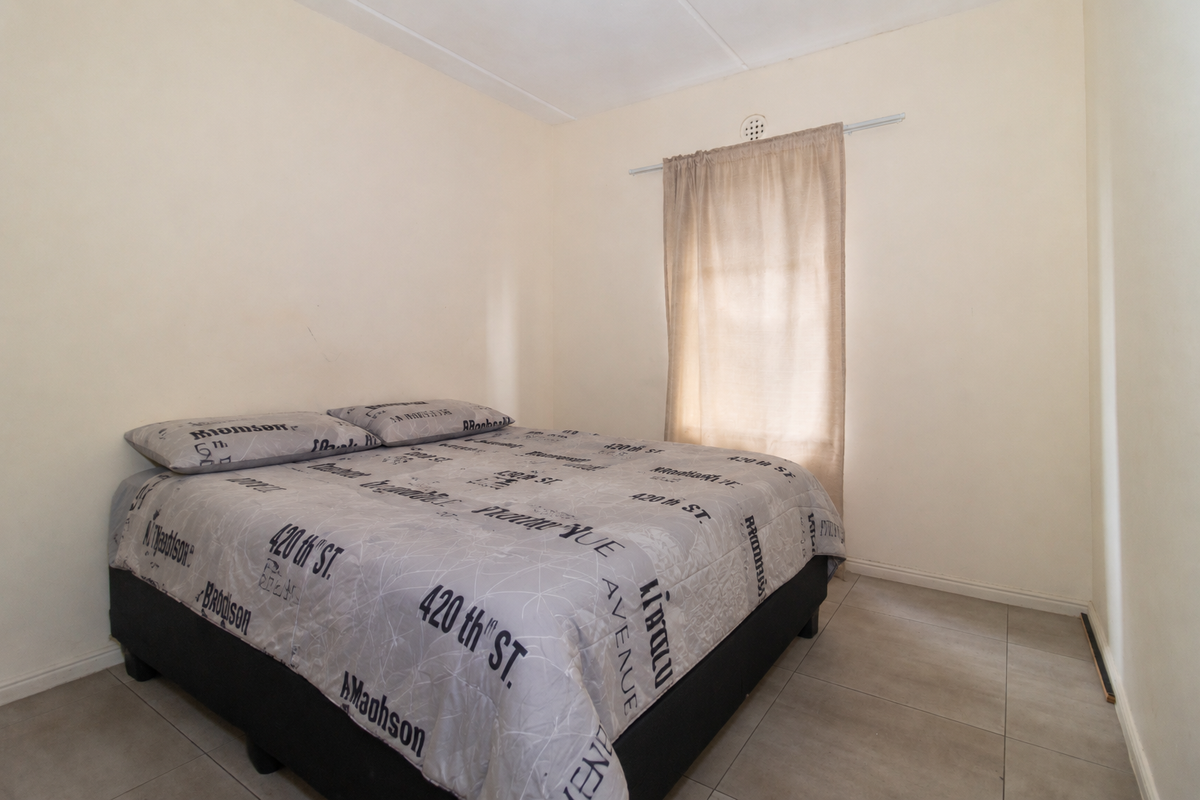 A simple bedroom featuring neutral wall finishes, tiled flooring, and a window with a curtain rail.