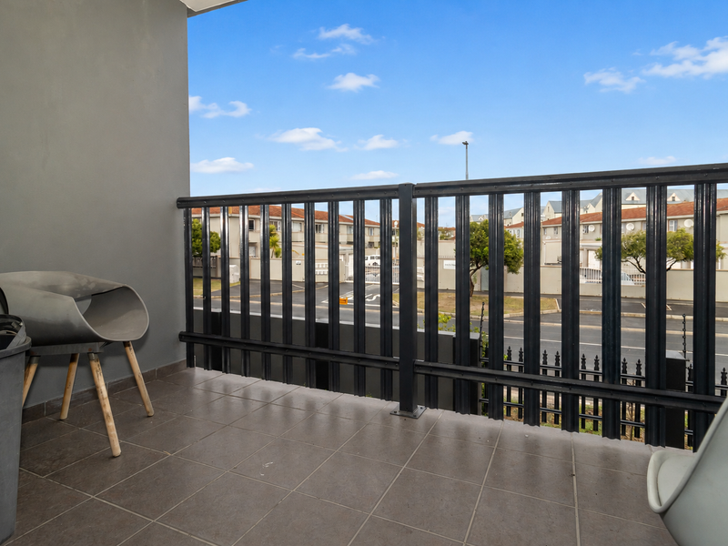 A private balcony featuring tiled flooring and a secure metal balustrade, offering an open view of the surrounding residential complex.
