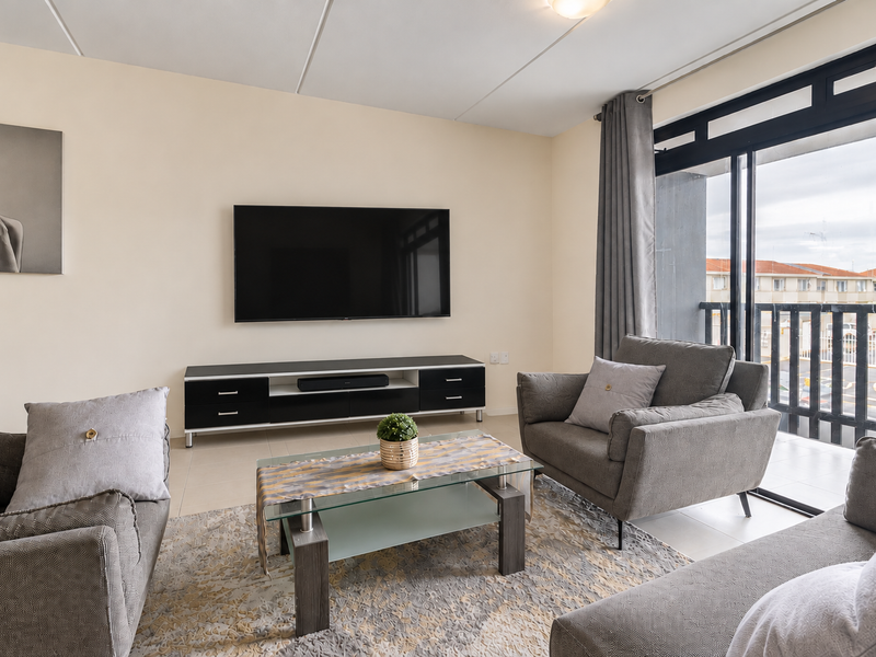 A well-lit living room featuring tiled flooring and a large sliding glass door providing access to the balcony.