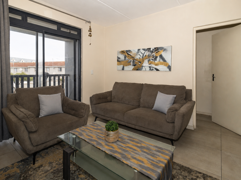 A comfortable living room featuring tiled flooring and a large sliding glass door that provides access to an outdoor balcony area.