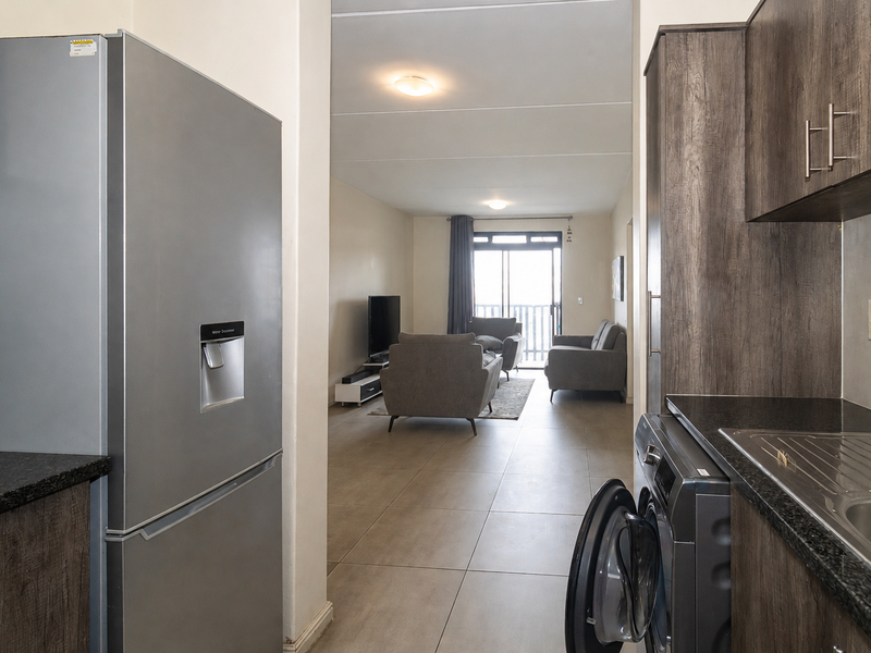 Open plan kitchen and living area featuring modern dark wood cabinetry, granite countertops, tiled flooring, and direct access to a balcony.