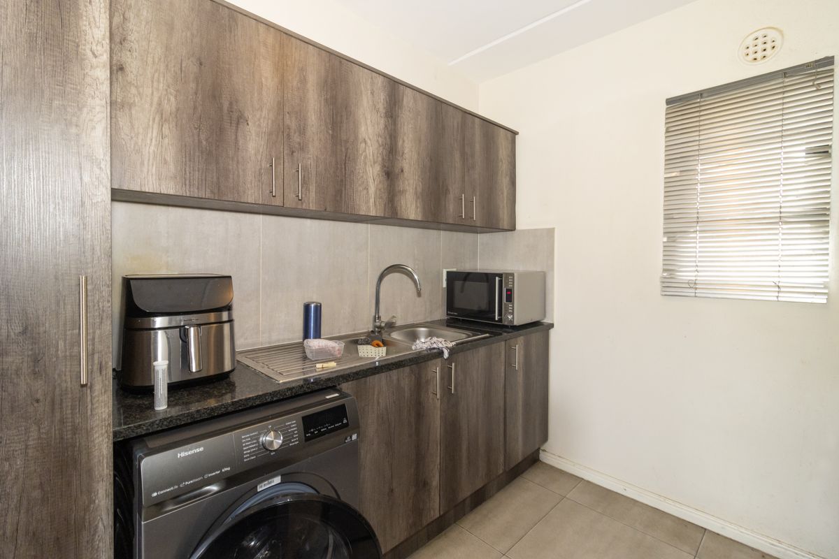 Compact kitchen featuring wood-look laminate cabinetry, granite countertops, stainless steel sink, and integrated laundry plumbing, offering a functional and efficient workspace.
