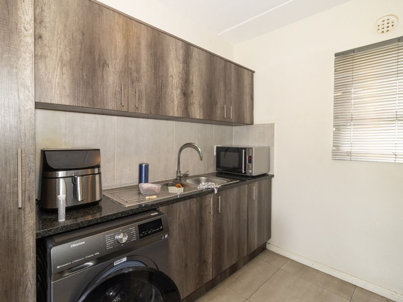 Compact kitchen featuring wood-look laminate cabinetry, granite countertops, stainless steel sink, and integrated laundry plumbing, offering a functional and efficient workspace.