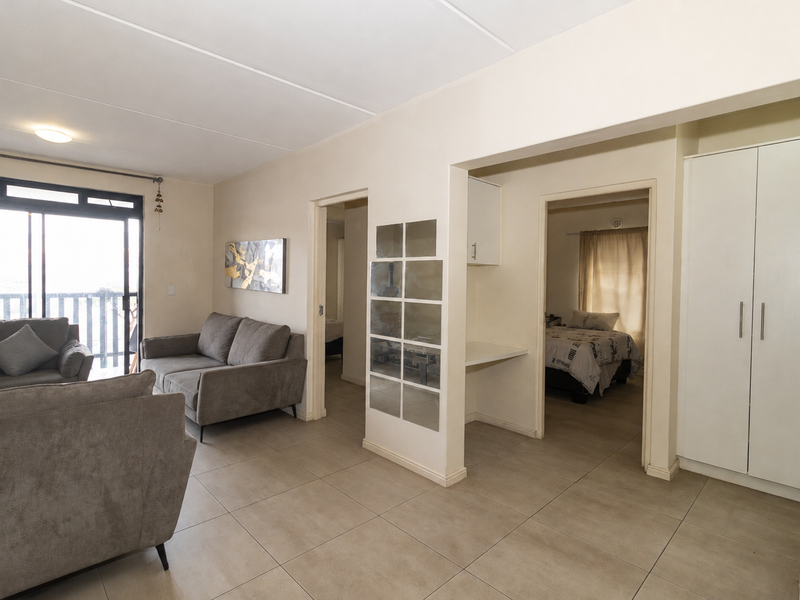 Open plan living area featuring tiled floors, built-in storage, and a sliding door leading to a balcony, with direct access to adjacent bedroom spaces.
