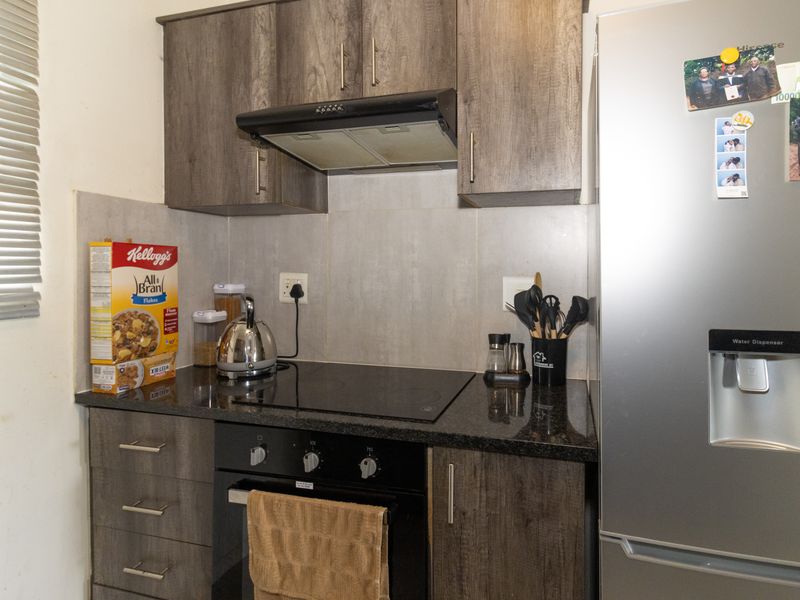 A compact kitchen featuring dark wood-look cabinetry, granite countertops, a built-in oven with an electric hob, and a tiled splashback.