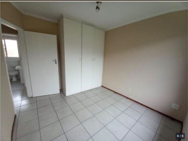 A clean, empty bedroom featuring neutral tiled flooring and built-in white cupboards, with an adjacent view into a bathroom.