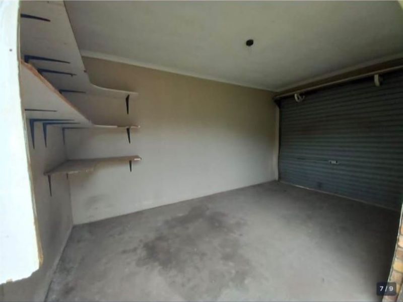 A functional garage space featuring a roller shutter door and built-in wall shelving, providing ample storage or vehicle parking potential.