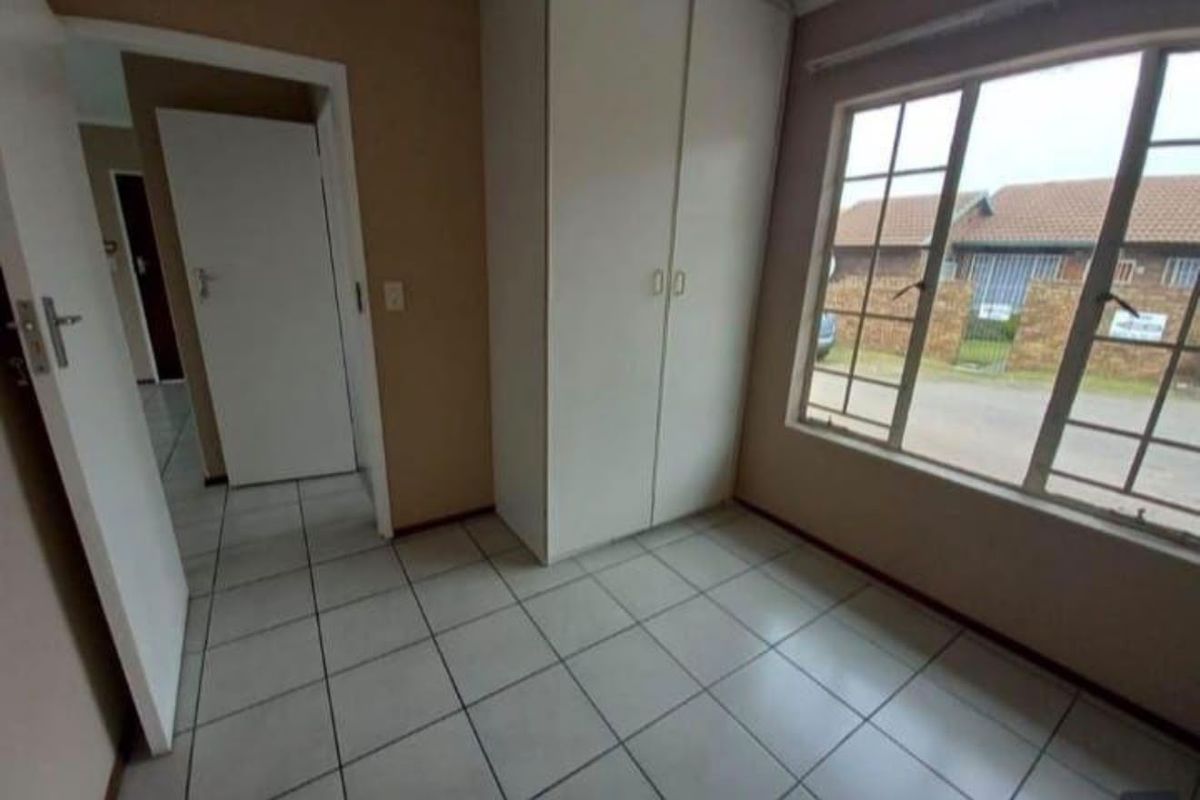 A simple, empty bedroom featuring tiled flooring, a built-in wardrobe, and a large window providing natural light.
