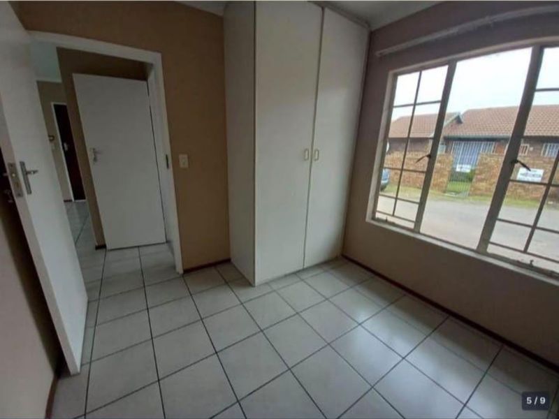 A simple, empty bedroom featuring tiled flooring, a built-in wardrobe, and a large window providing natural light.