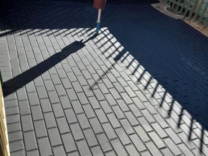 A clean, freshly paved outdoor patio area featuring dark brick pavers, enclosed by a brick boundary wall and metal fencing.