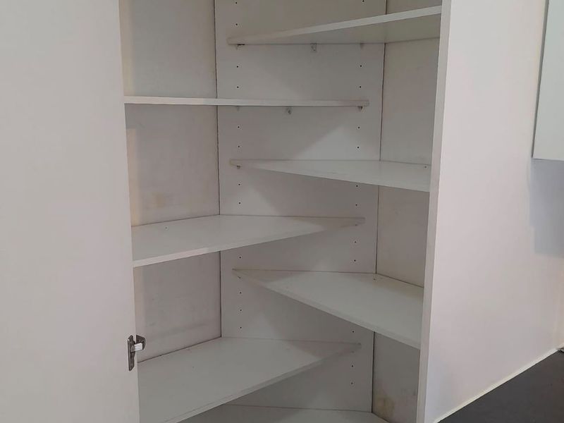 A built-in corner pantry or storage cupboard featuring adjustable white shelving and laminate finish.