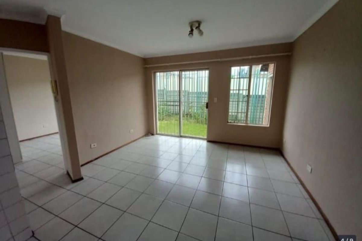 An empty, neutrally painted living room featuring tiled flooring and a sliding glass door with security bars leading to the exterior.