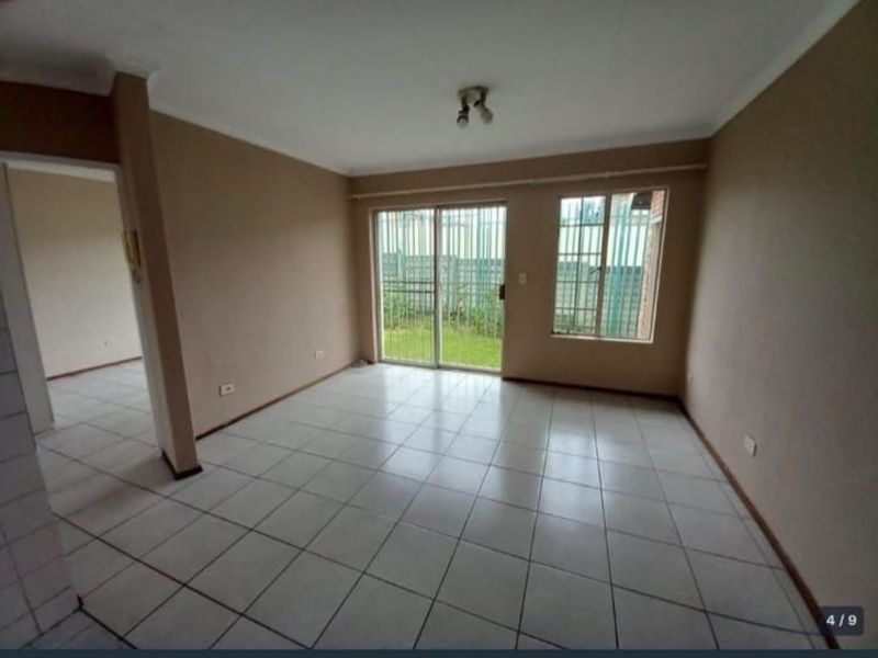 An empty, neutrally painted living room featuring tiled flooring and a sliding glass door with security bars leading to the exterior.