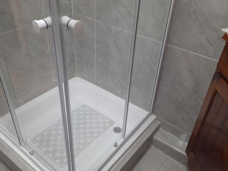 A modern bathroom featuring a glass-enclosed shower with grey tiled walls and a wooden vanity cabinet.