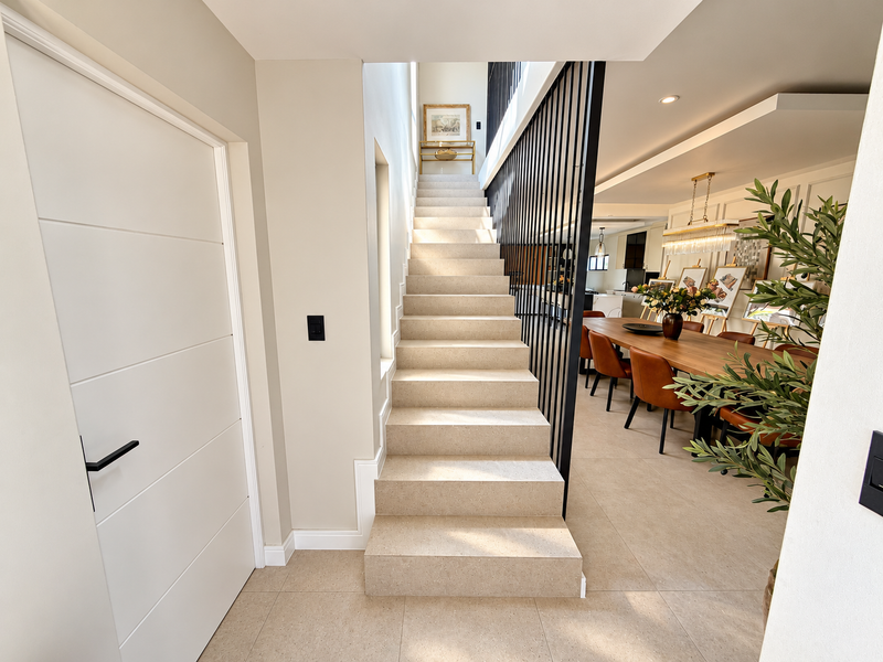 Modern entrance hall featuring a stone staircase with a sleek black metal balustrade, leading into an open-plan living and dining area with tiled floors.