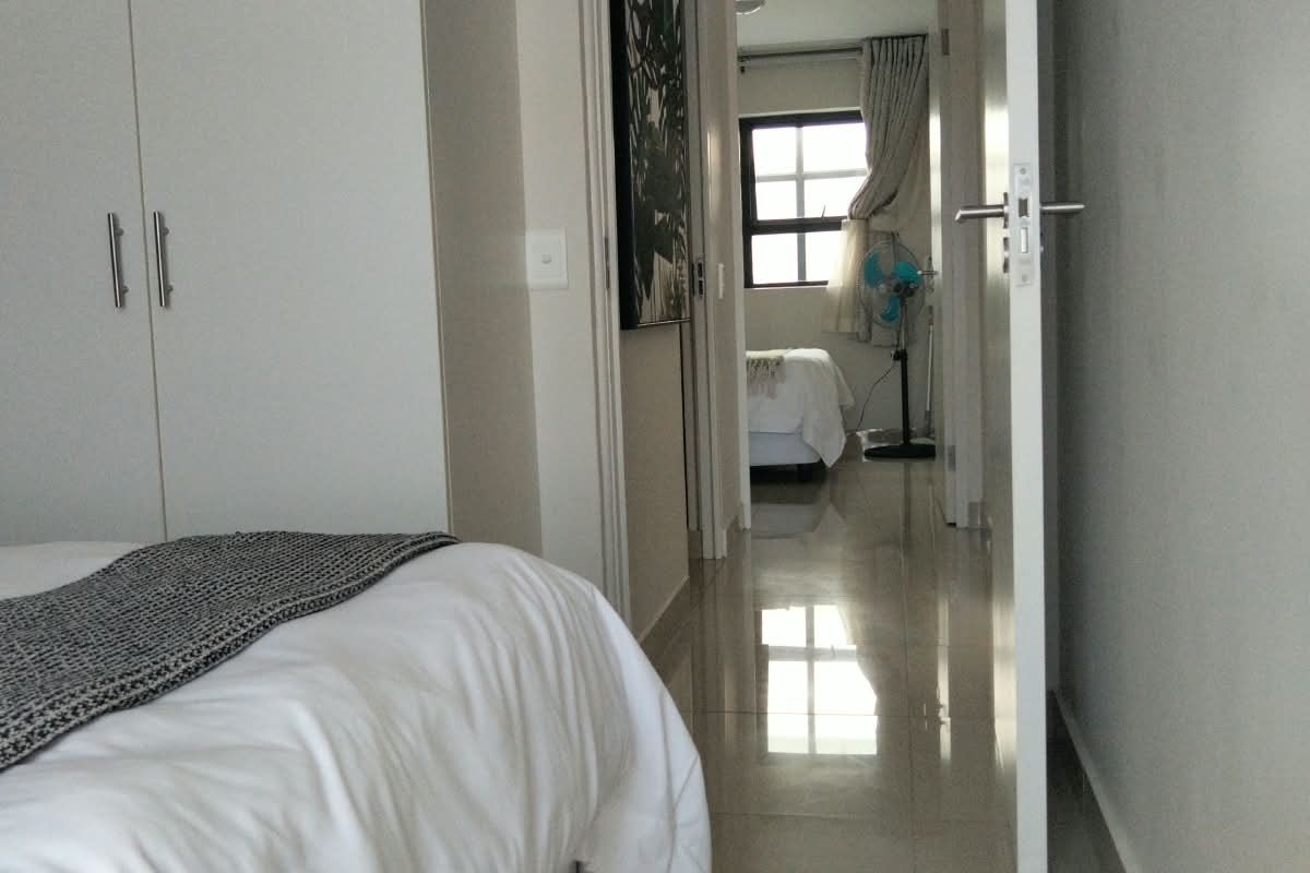 A bedroom featuring built-in cupboards and tiled flooring, with a view through the doorway into an adjacent room.