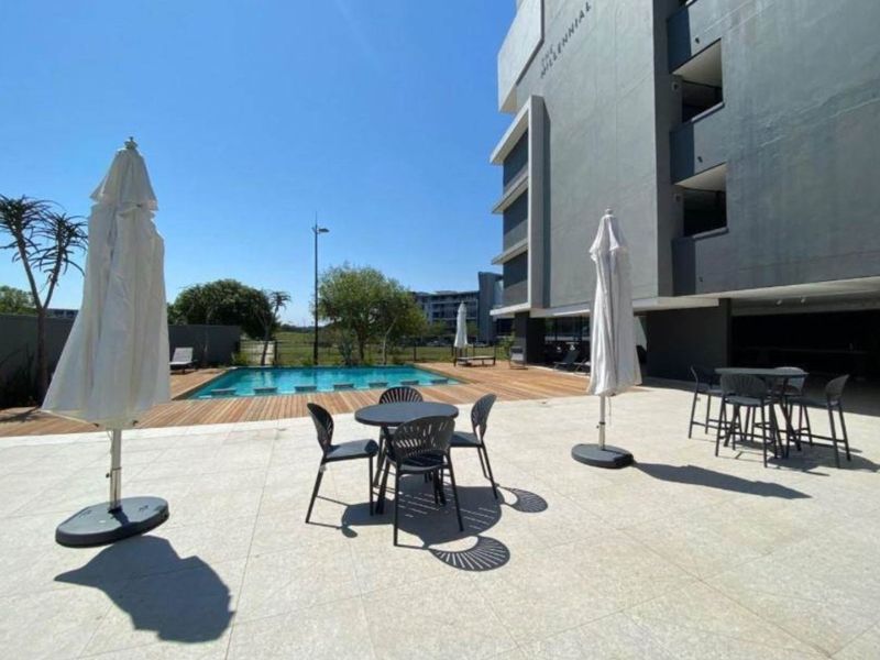 Modern apartment complex pool area featuring a swimming pool, wooden decking, and a spacious tiled patio for outdoor relaxation.