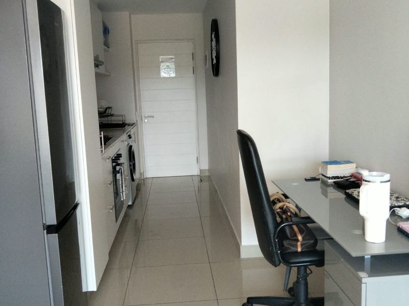 A compact kitchen area featuring modern cabinetry, tiled flooring, and integrated appliances, leading to a hallway entrance.