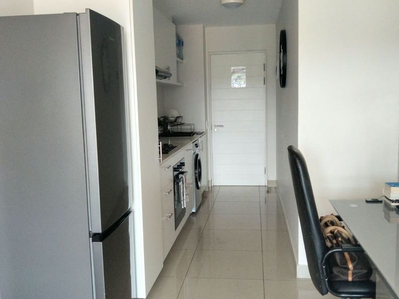 Compact kitchen area featuring modern white cabinetry, integrated oven, hob, and tiled flooring, with a functional layout including laundry appliance connections.