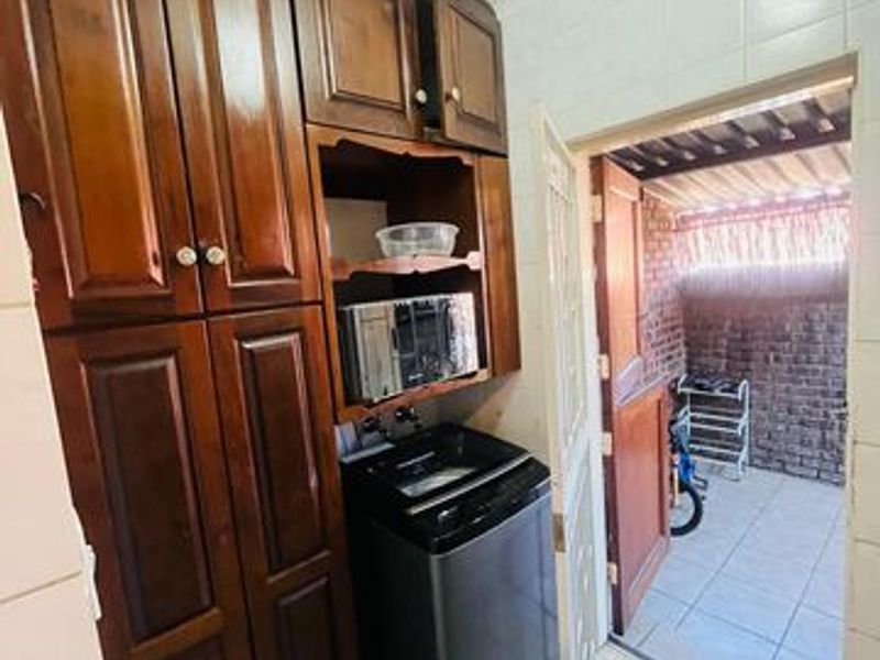 A functional laundry area featuring built-in wooden cabinetry and tiled finishes, with direct access to an outdoor courtyard space.