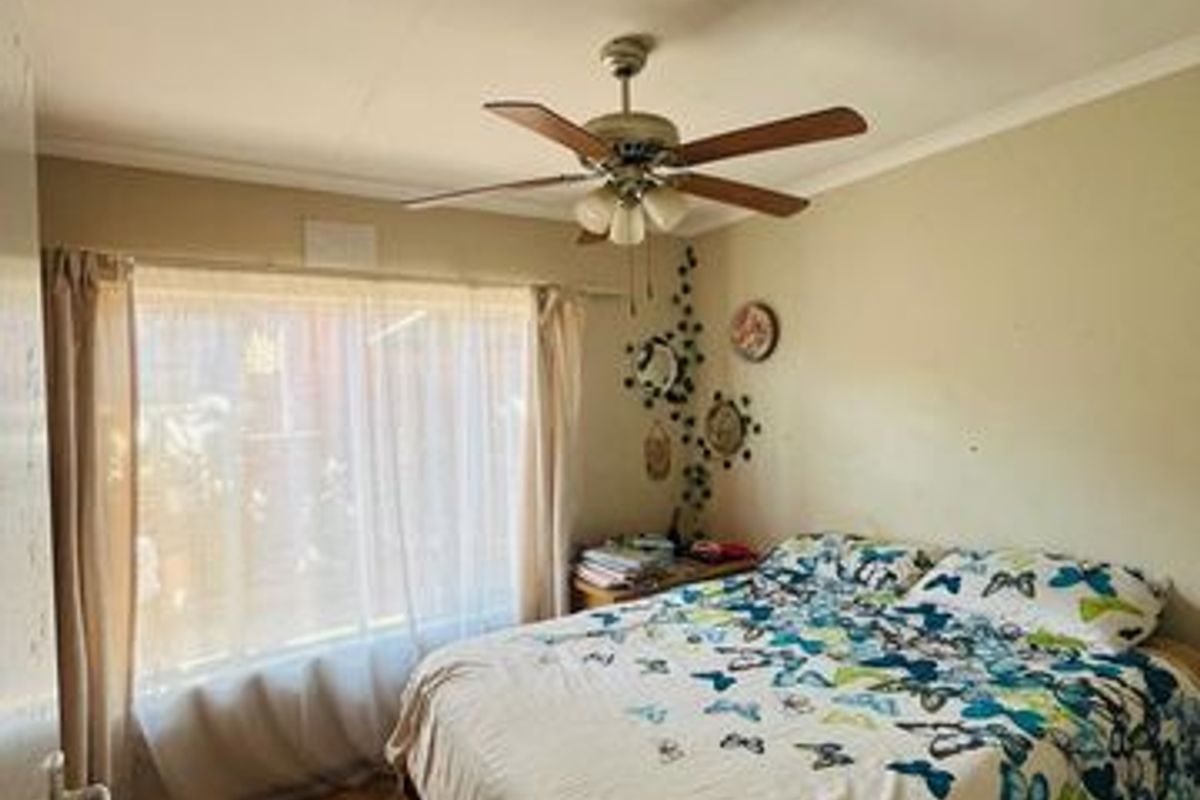 A standard bedroom featuring laminate flooring, a ceiling fan, and neutral wall finishes, offering a functional space ready for cosmetic updates.