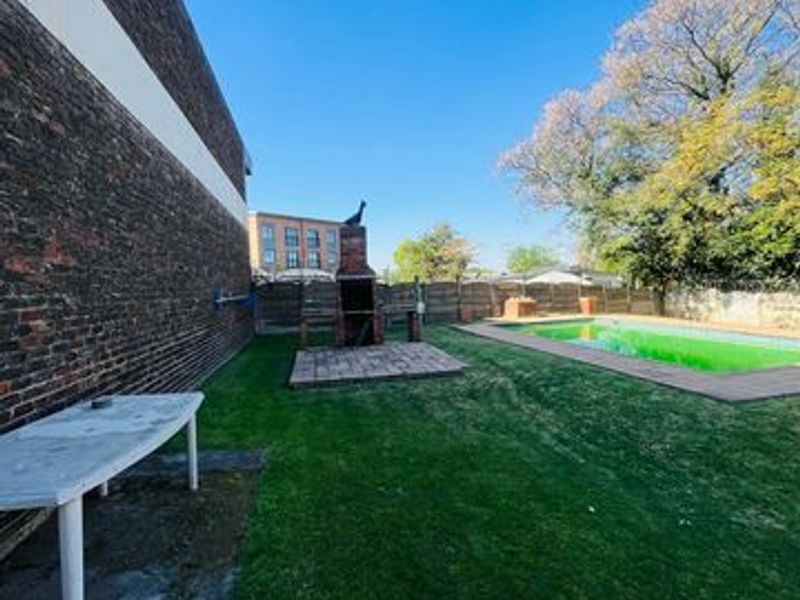 Outdoor pool area featuring a lawn, brick built-in braai, and perimeter fencing, offering a functional space for outdoor recreation.