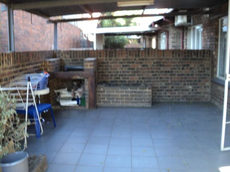A covered outdoor patio area featuring a built-in brick braai and tiled flooring, offering a functional space for outdoor entertainment.