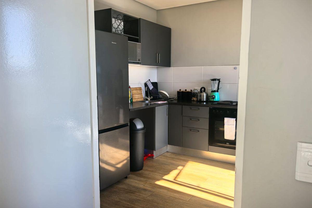 A compact, modern kitchen featuring dark grey cabinetry, laminate countertops, a built-in oven, and a tiled backsplash with wood-look flooring.
