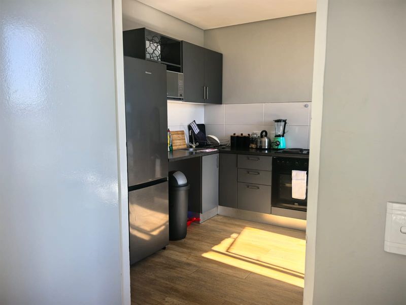 A compact, modern kitchen featuring dark grey cabinetry, laminate countertops, a built-in oven, and a tiled backsplash with wood-look flooring.