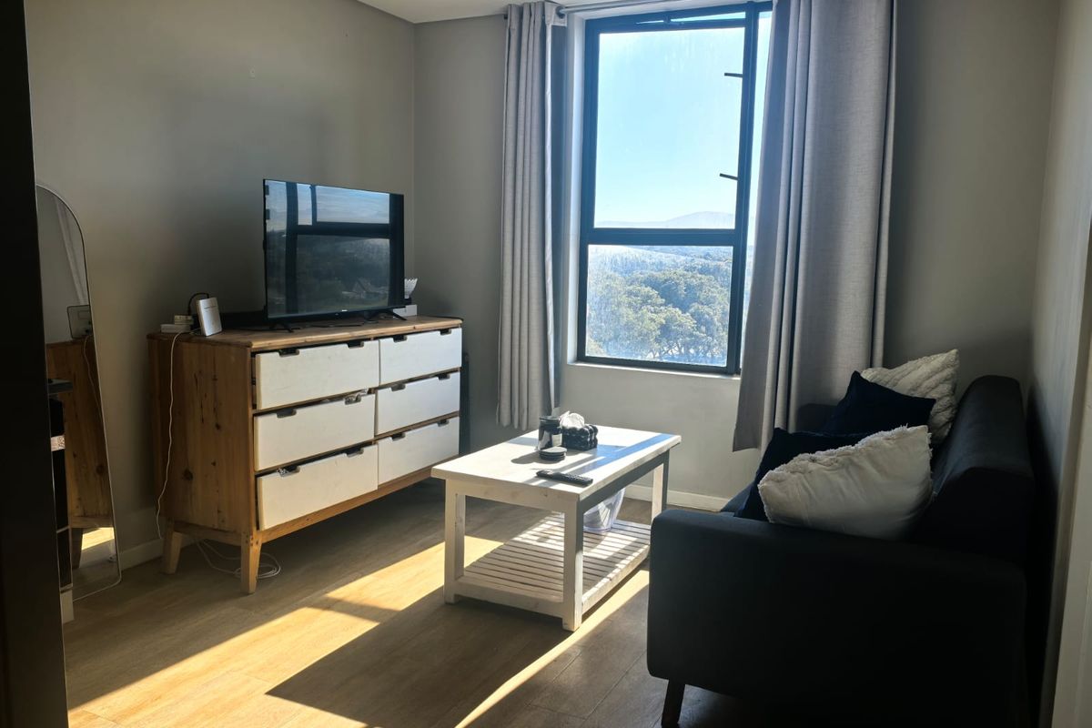 A bright living room featuring laminate flooring and a large window with natural light and scenic views.