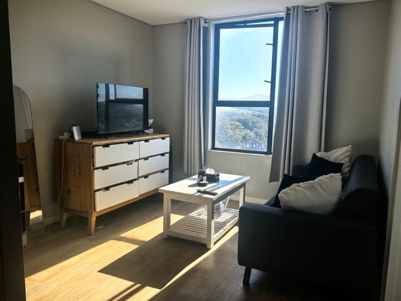 A bright living room featuring laminate flooring and a large window with natural light and scenic views.