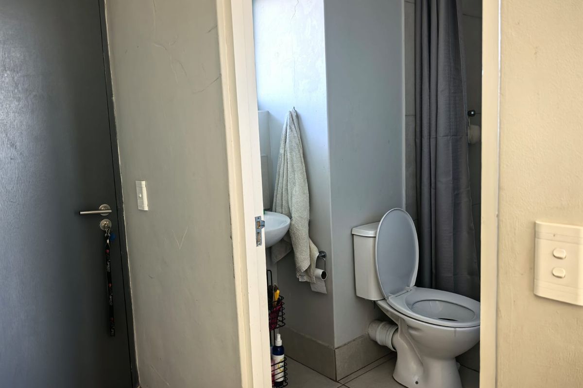 A compact bathroom featuring a standard toilet, washbasin, and tiled flooring, currently showing signs of wear and visible plumbing.