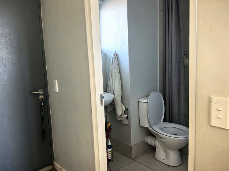 A compact bathroom featuring a standard toilet, washbasin, and tiled flooring, currently showing signs of wear and visible plumbing.