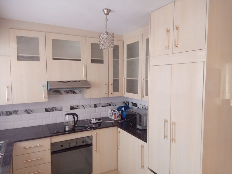 A functional kitchen featuring light-toned cabinetry, dark granite countertops, a subway tile backsplash, and integrated appliances including an oven and extractor fan.