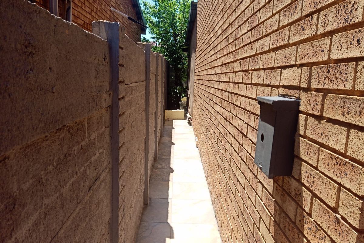 A narrow side passage featuring a tiled walkway between a brick townhouse wall and a precast concrete boundary wall.