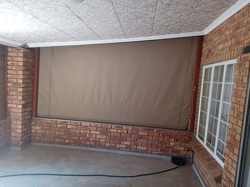 Covered patio area featuring face brick walls, tiled flooring, and a retractable canvas blind, providing a versatile outdoor space.