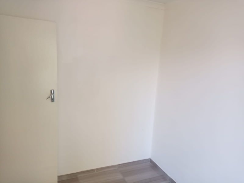 A clean, empty bedroom featuring neutral white walls and modern laminate flooring, providing a blank canvas for personalization.
