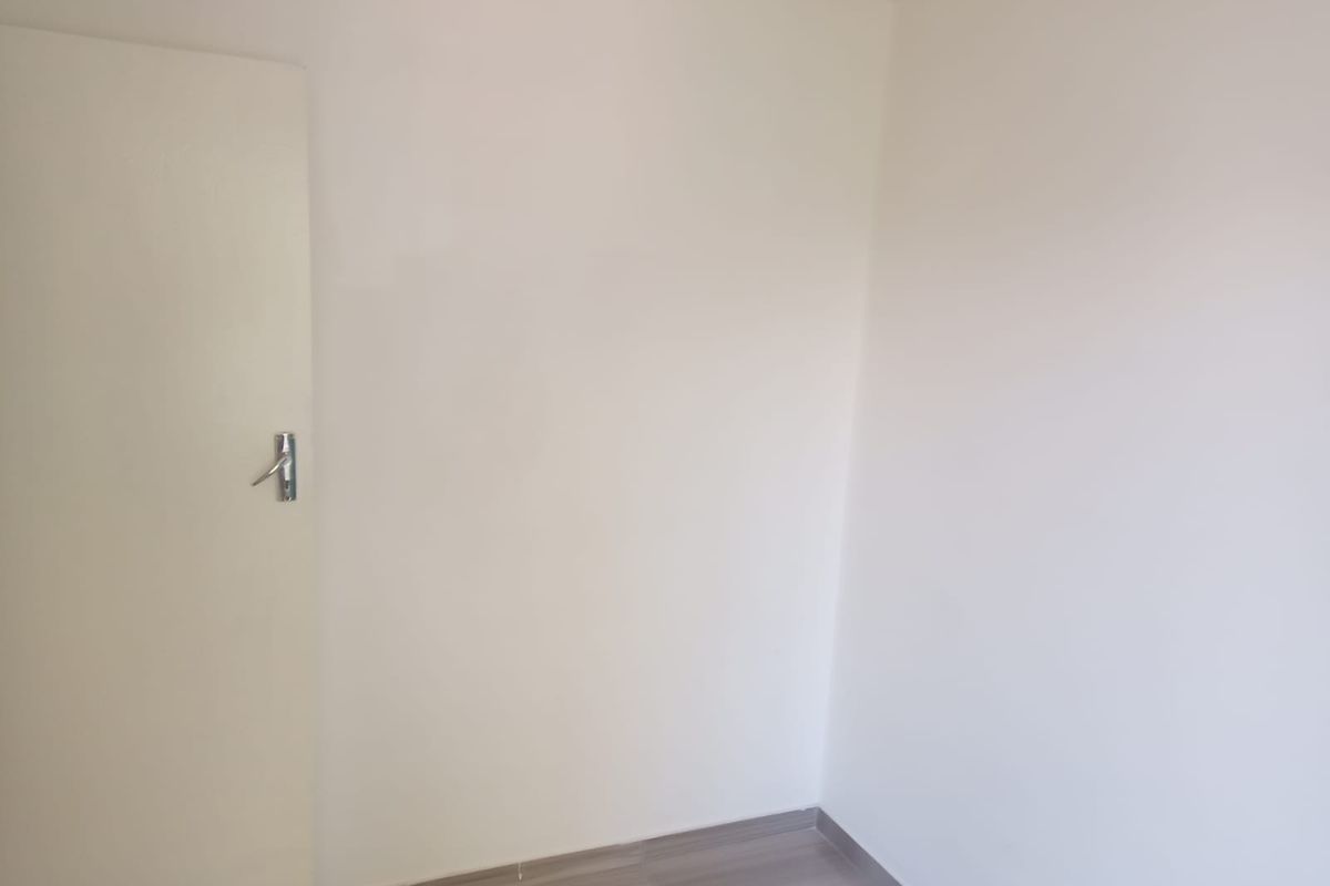 A clean, empty bedroom featuring neutral white walls and modern laminate flooring, providing a blank canvas for personalization.
