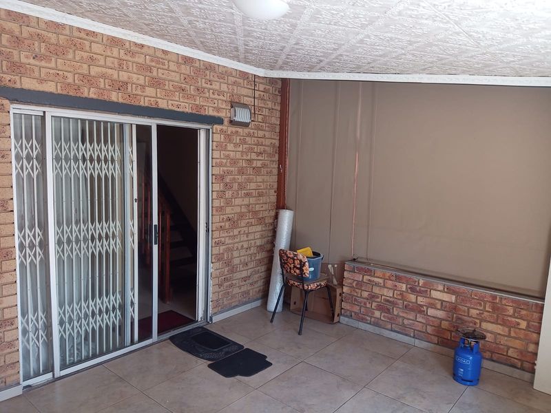 A covered patio area featuring exposed brick walls, tiled flooring, and a sliding glass door with a security gate.
