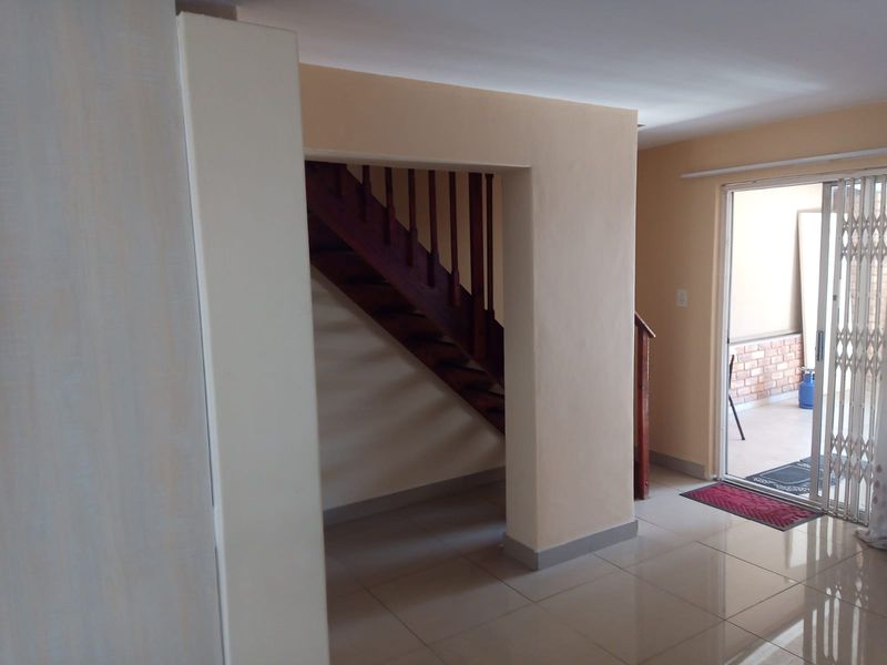A bright hallway featuring a wooden staircase and a sliding glass door with a security gate leading to an outdoor patio area.