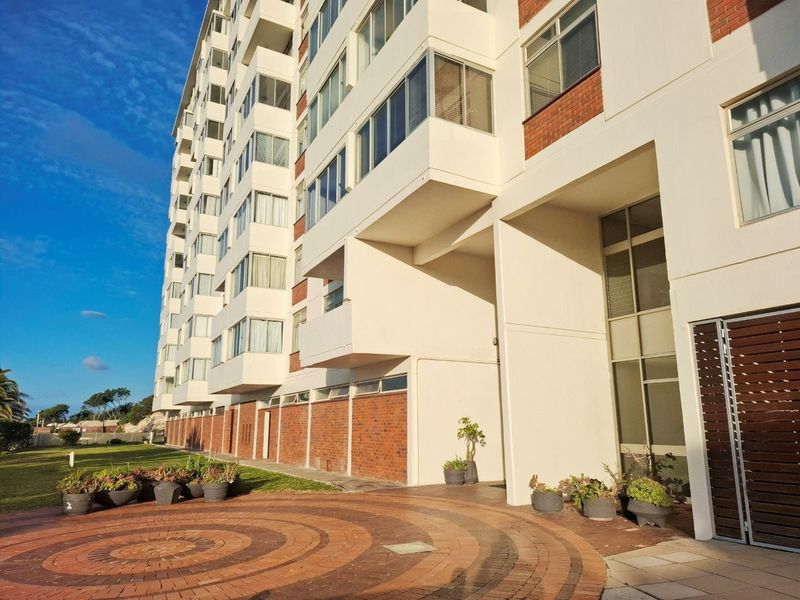 A view of the rear apartment building facade featuring brick detailing, multiple balconies, and a paved courtyard area.