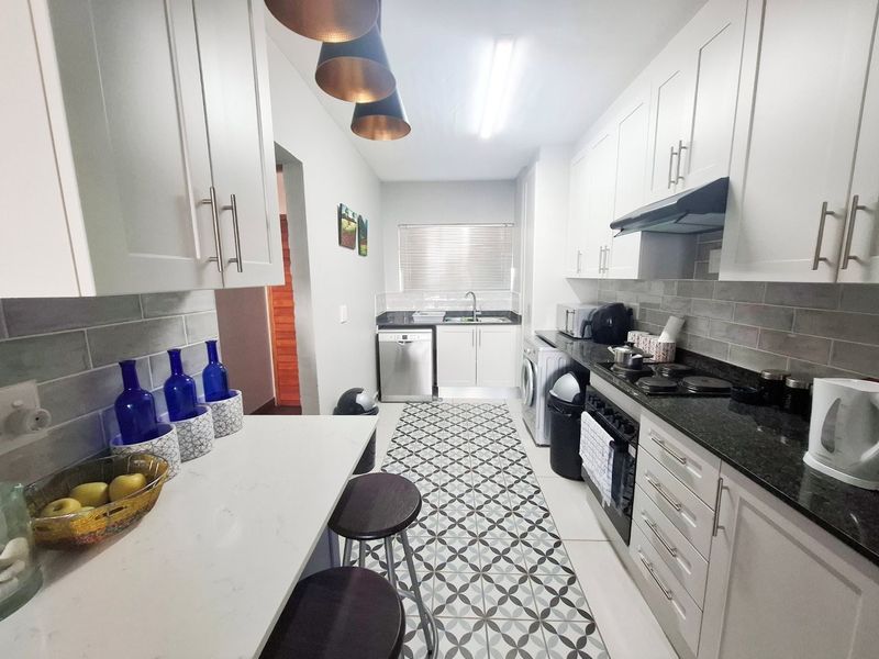 Modern galley-style kitchen featuring white cabinetry, dark stone countertops, subway tile backsplash, and stylish patterned floor tiles with integrated appliances.