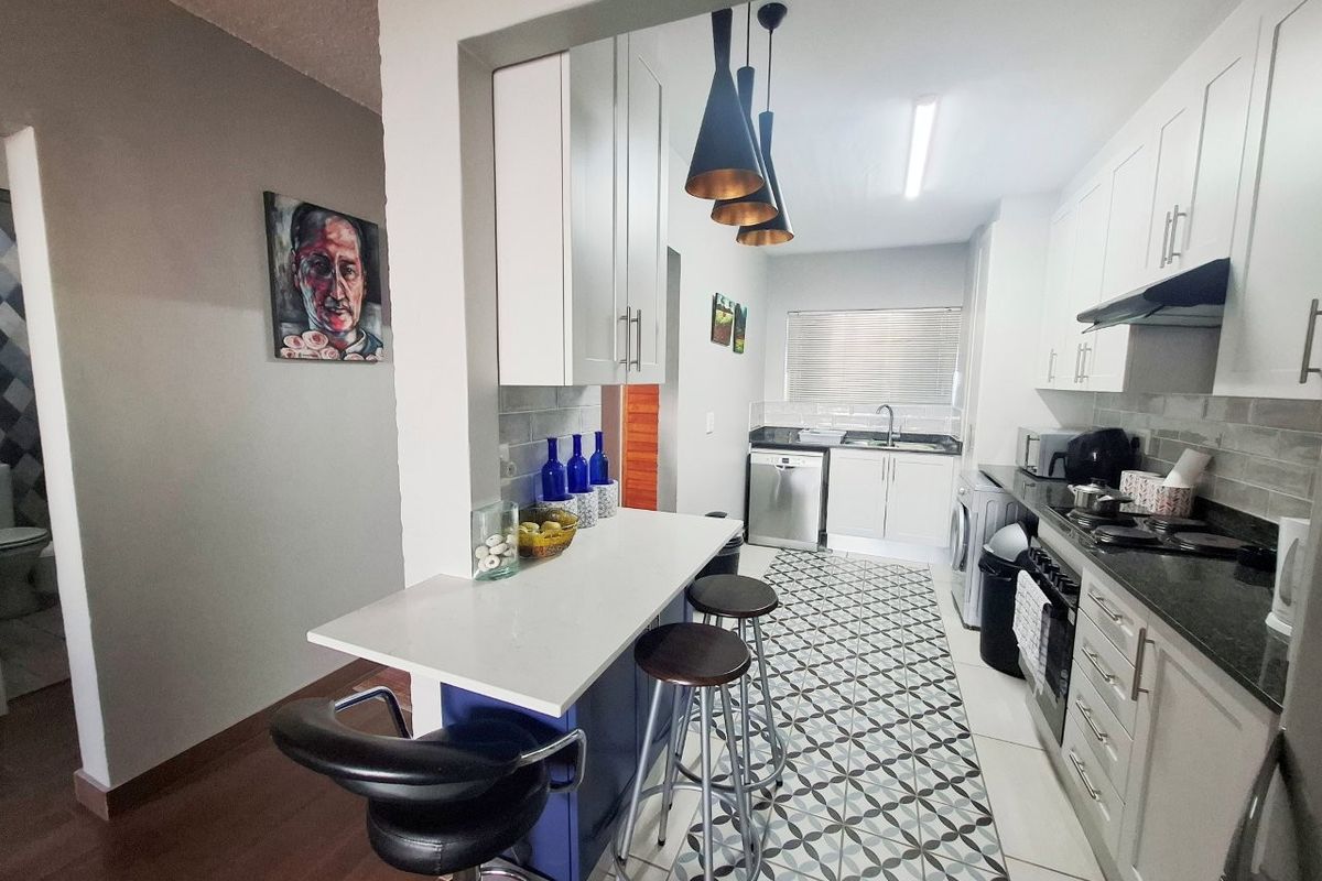 Modern kitchen featuring white cabinetry, stone countertops, a breakfast bar, and patterned floor tiles, offering a functional and stylish cooking space.