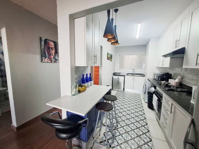 Modern kitchen featuring white cabinetry, stone countertops, a breakfast bar, and patterned floor tiles, offering a functional and stylish cooking space.