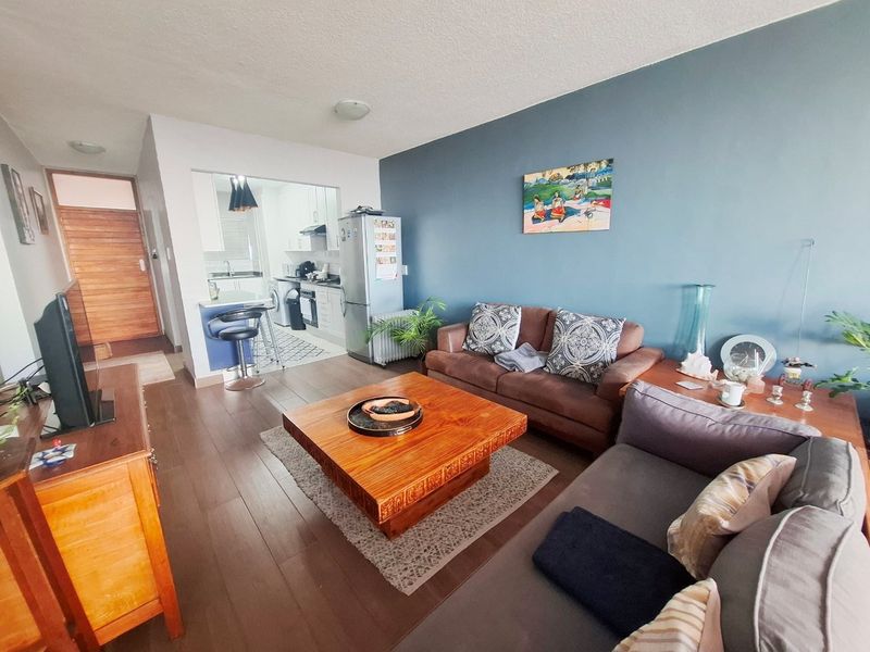 Open plan living area featuring laminate flooring and a connected kitchen with built-in cabinetry, oven, and hob.