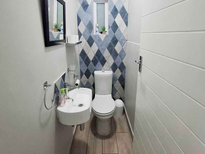 A compact, modern bathroom featuring a wall-mounted basin, toilet, and a decorative diamond-patterned tiled feature wall.