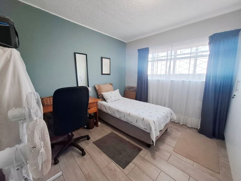 A functional bedroom featuring tiled flooring and a window fitted with security bars, offering a neutral space ready for personalization.